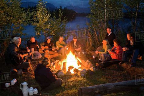 Group Of Adults Sitting Around A Campfire Sing And And Talk As They