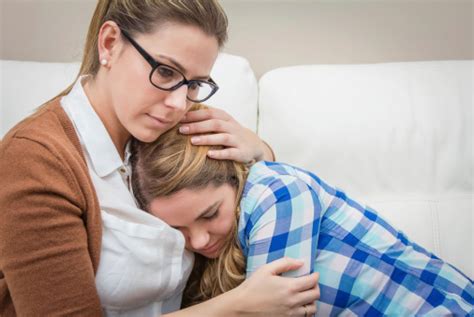Mother Hugging Her Upset Daughter On White Settee Stock Photo