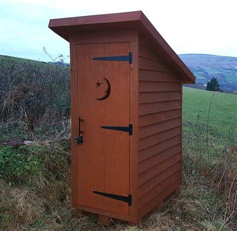 A Wooden Outhouse In The Middle Of A Field With A Crescent On Its Door