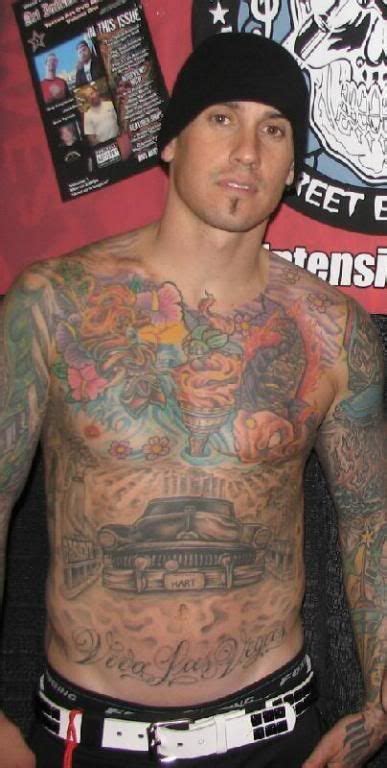A Man With Tattoos On His Chest Standing In Front Of A Wall Covered In