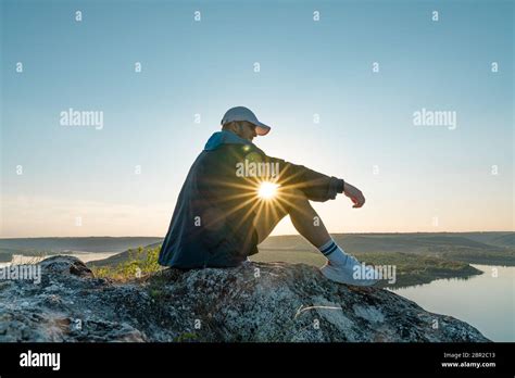Man Sitting On A Ledge Of A Mountain Enjoying The Beautiful Sunset