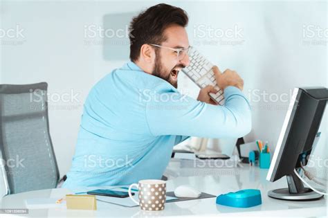 Angry Businessman Smashing Keyboard Into Monitor At Workplace Stock