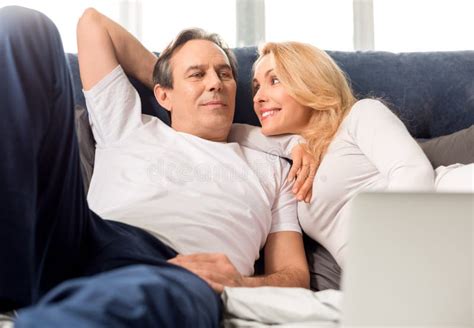 Middle Aged Couple Looking At Each Other And Lying On Bed At Home Stock