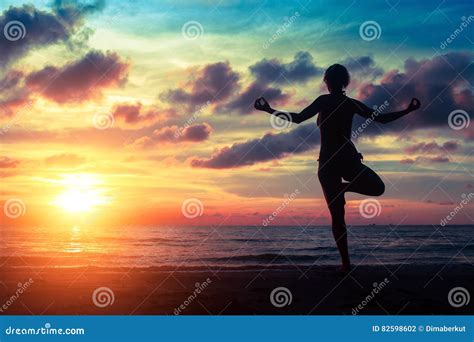 Silhouette Woman Practicing Yoga On The Beach At Sunset Stock Photo