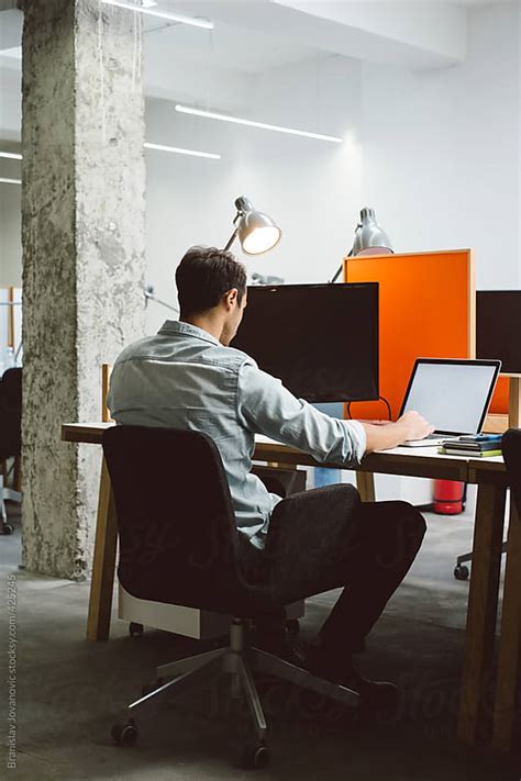 Man Sitting At His Desk And Working On A Laptop By Branislav Jovanović