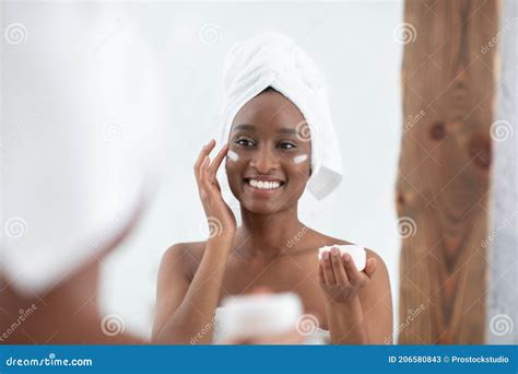 Smiling Cute Millennial African American Lady With Towel On Head After Shower Applying Cream On
