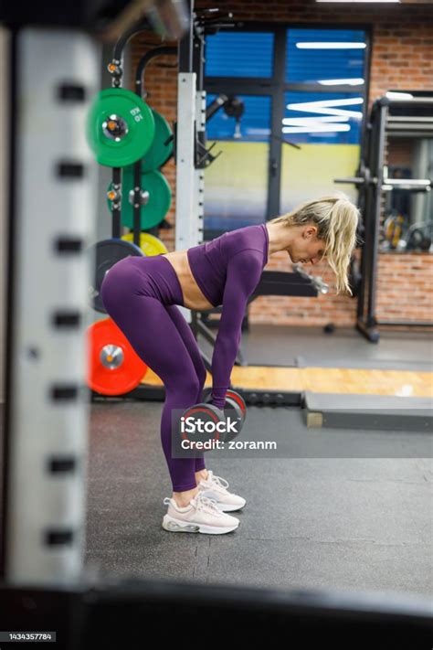 Woman Bending Over And Lifting Dumbbells In The Gym Stock Photo