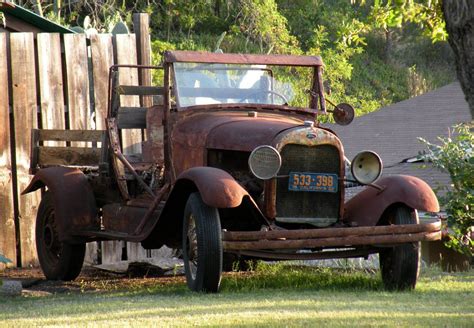 An Old Rusted Truck Is Parked In The Yard Next To A Wooden Fence And Tree