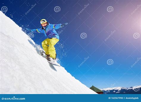 Guy Snowboarding Down The Mountain Slope Against Blue Sky Stock Photo