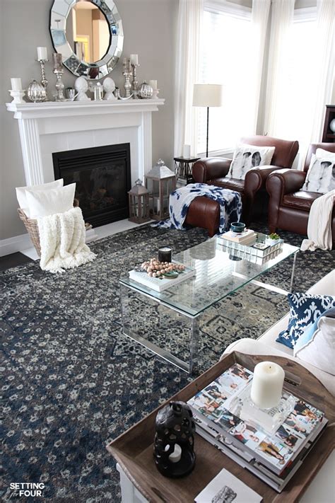 A stylish blue and gray living room features a gray sofa with swoop arms and blue pillows faces a black oak coffee table with two blue and one white complementing accent chairs and a round fluted capiz accent table, atop a dark gray diamond jute rug. An Indigo Blue Color Scheme For Our Living Room - Setting for Four