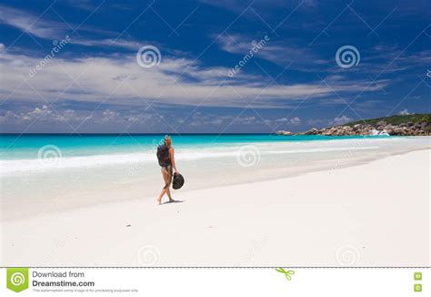 Blonde Woman With Backpack And Hat Walks Along A Beach