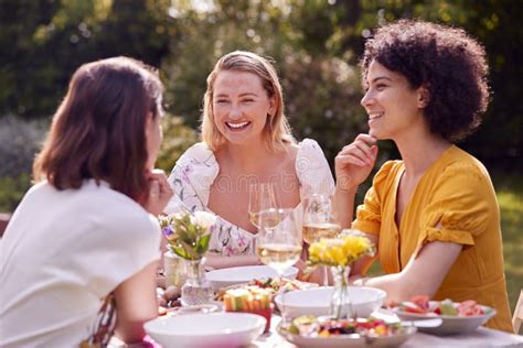 Three Female Friends Sitting Outdoors In Summer Garden At Home Eating