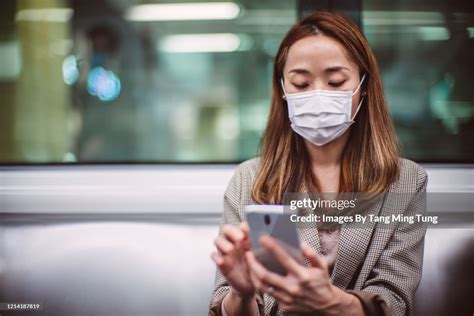 Young Asian Woman With Protective Face Mask Using Smartphone While Commuting In The City Riding