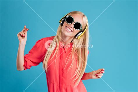 Portrait Of A Joyful Woman In Sunglasses Enjoying Music And Dancing Over Blue Background Royalty