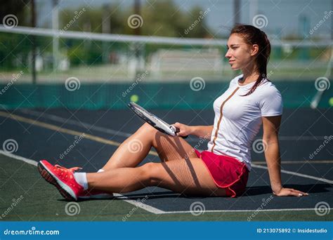 Caucasian Woman Sitting On A Tennis Court With A Racket In Her Hands On