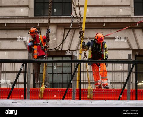 dos obreros con ropa de seguridad naranja y cascos vistos de pie e inspeccionando una viga de