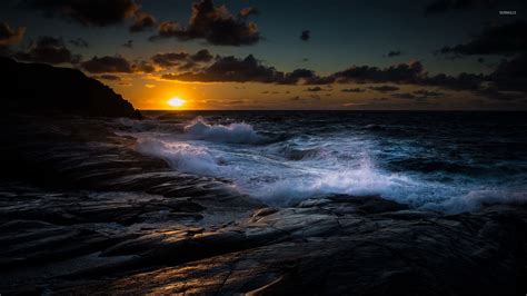 Waves Fighting With The Rocky Shore At Sunset Wallpaper