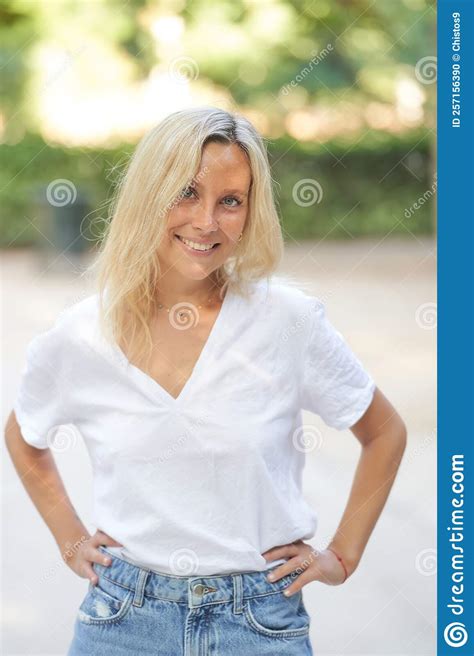 Woman Looking At The Camera And Smiling While Standing With Her Hands On Her Hips In A Park