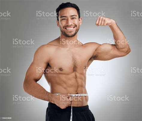 Studio Shot Of A Man Flexing His Muscles While Measuring His Waist
