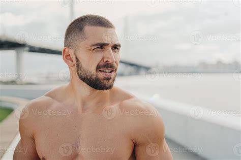 Outdoor Shot Of Bearded Man With Muscular Naked Torso Concentrated Into Distance Thinks About