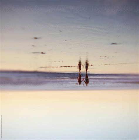 Image Of Two Silhouettes Walking On Beach Showing Upside Down View Del Colaborador De Stocksy