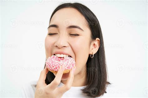 Close Up Of Smiling Pleased Asian Woman Eats Glazed Pink Doughnut Enjoys Eating Tasty Donnut