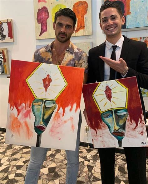 Two Men Holding Up Paintings In Front Of Them