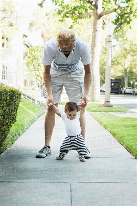 Father Helping Baby Son Walk On Sidewalk Stock Photo Dissolve
