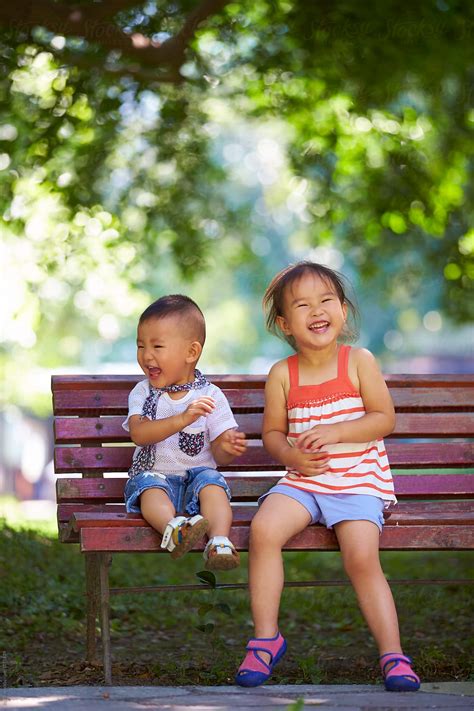 Two Lovely Kids Sitting On The Bench In The Park By Stocksy