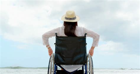 Rear View Of Disabled Woman Sitting With Arms Up On Wheelchair At Beach