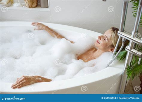 Top View On Young Blonde Attractive Female Lying In Hot Bathtub And Relaxing In Bubbles Stock