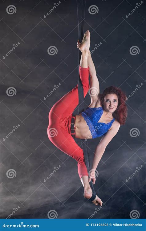female athletic and flexible aerial circus artist with redhead on aerial straps on black