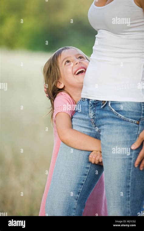 Cheerful Little Girl Hugging Her Mothers Leg In The Field Stock Photo
