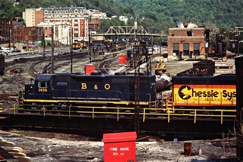 A Train Is On The Tracks In An Industrial Area With Buildings And Hills