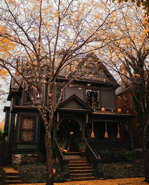 An Old Victorian Style House With Pumpkins On The Porch And Trees In