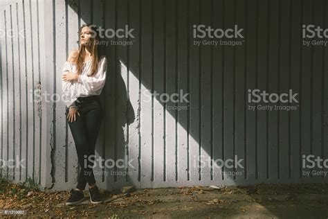 Attractive Brunette Leaning Against Wall Illuminated With Sunlight In
