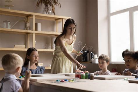 Pretty Young Artist Woman Teaching Diverse Group Of Little Kids Stock
