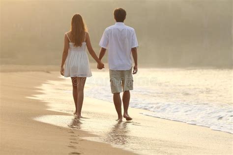 Couple Walking And Holding Hands On The Sand Of A Beach Back View Of A