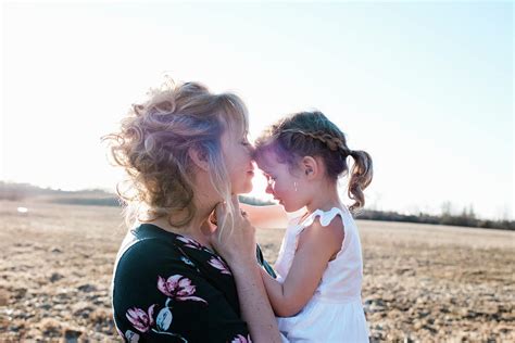 Mother Holding Daughter Cuddling And Smiling At Sunset In Summer