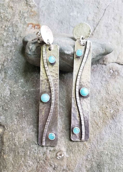Two Silver Earrings With Turquoise Stones On Them Sitting On Top Of A