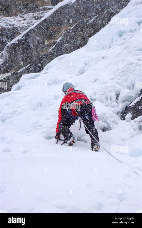 Male Ice Climber In Heavy Snowfall And Bad Weather Climbing A Frozen