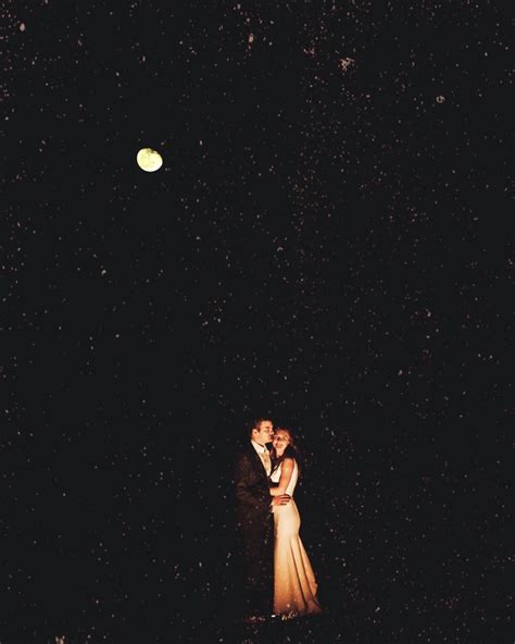 A Bride And Groom Standing In The Snow At Night Under A Full Moon With