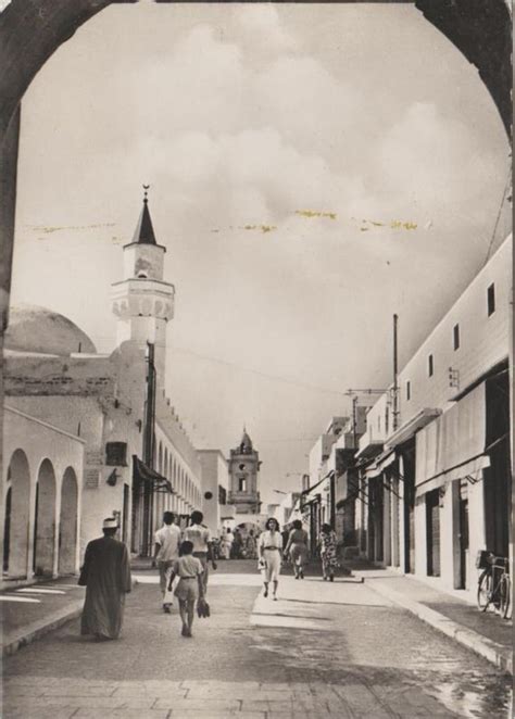 An Old Black And White Photo Of People Walking Down A Street With