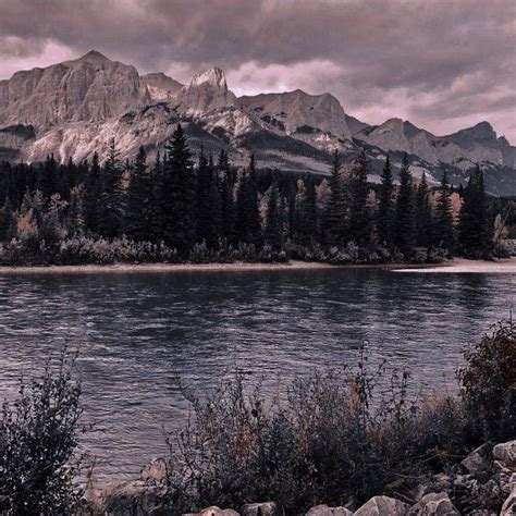 A Lake Surrounded By Mountains And Trees Under A Cloudy Sky With Rocks