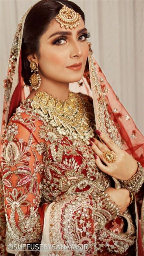a woman in a red and gold bridal outfit with jewelry on her head posing for the camera