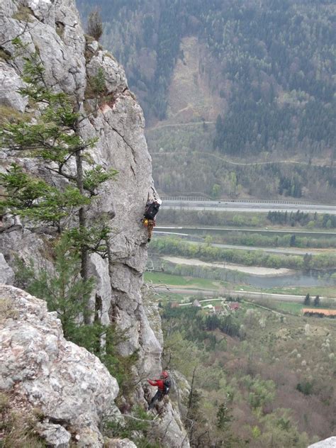 Two Climbers Climbing Up The Side Of A Rocky Cliff With Valley In The