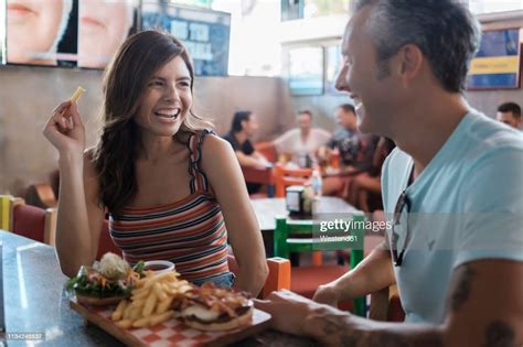Happy Couple Sharing Hamburger And French Fries In A Bar High Res Stock
