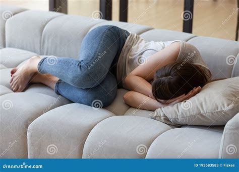 Frightened Young Woman Curled Up On Sofa In Fetal Position Stock Image