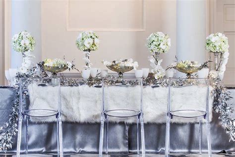 The Table Is Set With Silver Chairs And White Flowers In Vases On Top Of It