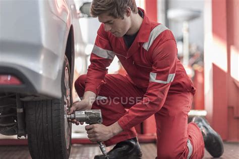 Car Mechanic At Work In Repair Garage Changing Tires Impact Driver